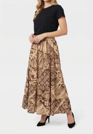 Vrouw draagt een zwart topje met korte mouwen, een lang beigebruine rok met patroon hoog in de taille en zwarte hoge hakken.