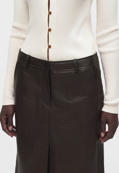 Cardigan crème côtelé avec boutons marron associé à une jupe en cuir marron foncé taille haute, montré de la taille à mi-cuisse.