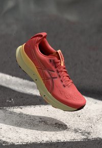 Baskets de course avec une tige rouge, une semelle jaune et un design en maille texturée. Comprend des lacets et des accents de logo sur le côté.