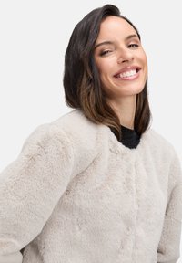 Lys beige faux fur jakke med rund hals, blød tekstur og let oversized pasform, med en subtil glans og ingen synlig hardware.