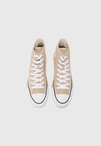 Beige hochgeschnürte Sneaker aus Canvas mit weißen Schnürsenkeln, Gummikappe und schwarzem Sohlenrand. Auf der Seite befindet sich ein runder Logo-Patch.