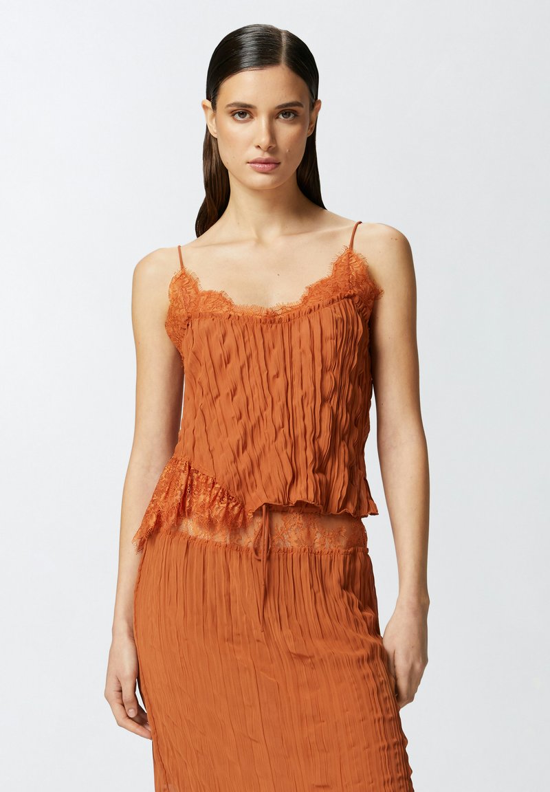 Narandžasti nabrani top s čipkastim rubom, koji ima tanke naramenice i lepršavu siluetu. Materijal ima mekan, teksturiran završetak.