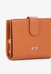 Portafoglio in pelle arancione con texture, dotato di pattella ripiegabile, accessori in tonalità oro e logo impresso. Design compatto con più slot per carte.
