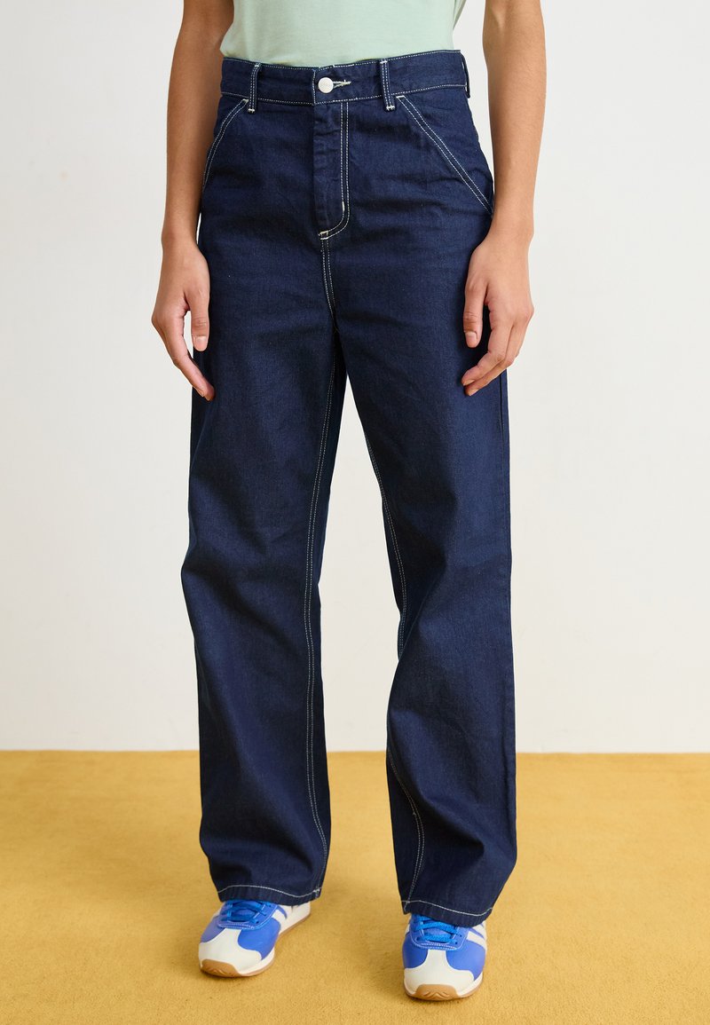 Mörkblå denim breda byxor med synliga vita sömmar, hög midja och framfickor, kombinerat med blå sneakers för träning.