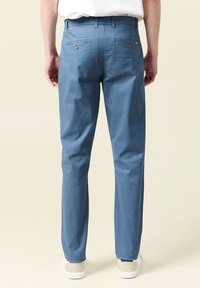 Ljusblå byxor med rak passform, tillverkade av ett slätt tyg. Har två bakfickor med knäppning och ett midjeband.