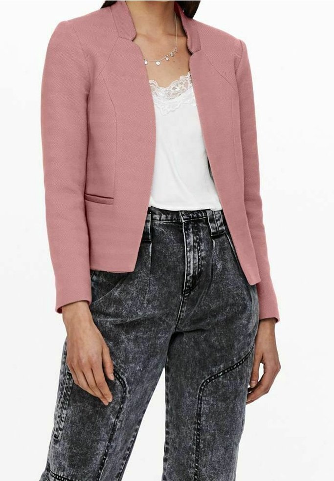 Veste texturée rose blush avec une coupe ajustée, un col montant et des coutures aux épaules, associée à un haut en dentelle blanche et un jean noir déchiré.