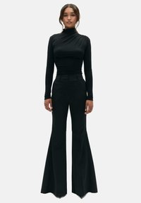 Schwarzes Langarmoberteil mit hohem Kragen und geraffter Textur, kombiniert mit hochtaillierten schwarzen Schlaghosen. Glatter Stoff, minimalistisches Design.