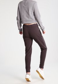 Šedý zkrácený svetr s dlouhými rukávy, v kombinaci s tmavě hnědými úzkými joggery s bočními zipovými kapsami a bílými teniskami se stříbrnými akcenty.