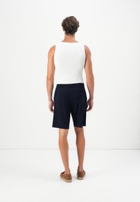 Tengerész kék, laza szabású rövidnadrág, elasztikus derékkal, fehér ujjatlan topot és barna slip-on cipőt viselve. Egyszerű, minimalista dizájn.