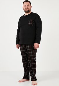 Sort langærmet skjorte med en brystlomme, der har en rød ternet mønster, parret med sorte pyjamasbukser, som viser et rødt og hvidt ternet design.
