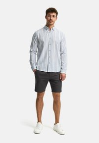 Camisa de botonadura en rayas blancas y azul claro, de mangas largas, con cuello y botones marrones; combinada con pantalones cortos oscuros y zapatillas blancas.