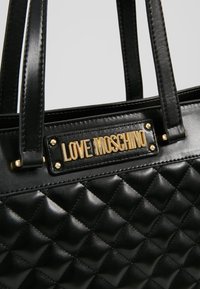 Sac à main en cuir noir matelassé avec deux poignées et plaque de marque dorée "Love Moschino" sur le devant supérieur.