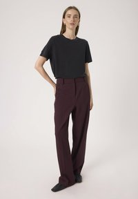 Schwarzes Kurzarm-T-Shirt kombiniert mit hoch taillierten weinroten Hosen. Die Hosen haben einen maßgeschneiderten Schnitt und weite Beine. Schwarze flache Schuhe runden den Look ab.