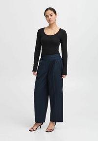 Musthave mustrõhuvalge pikkade varrukatega topp, millel on ümar lõhk, sobitub tumesiniste laia jala pükstega, millel on voltid. Riietuse lõpetavad kitsaste rihmadega mustad sandaalid.
