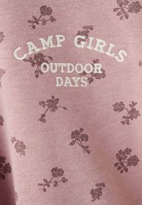 Tessuto rosa con un motivo floreale in tonalità più scure. La scritta "CAMP GIRLS OUTDOOR DAYS" è in bianco, centrata sul material.