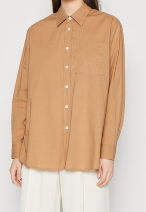 Chemise à manches longues en tissu marron clair, col classique, poche poitrine unique et boutons blancs sur le devant.