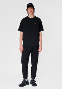 Svart t-shirt med korta ärmar, rund halsringning och logotyp, kombinerad med svarta joggerbyxor med elastiska muddar och dragsko i midjan.