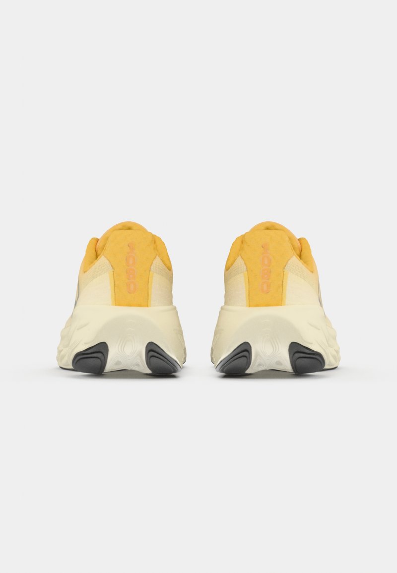 Un par de zapatillas amarillas y beige con suelas blancas gruesas vistas desde atrás sobre un fondo blanco liso.
