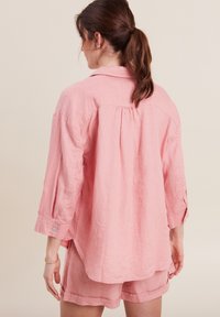 Camicia di lino rosa chiaro con colletto, maniche a 3/4 e dettaglio plissettato sulla schiena, abbinata a pantaloni corti coordinati in un tessuto morbido.