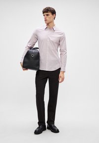 Lichtroze gestreepte shirt, zwarte leren tas met een zilverkleurig accent, donkere broek en zwarte schoenen. Schoon design met een getailleerde pasvorm.