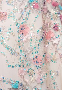 Tissu transparent avec une broderie argentée complexe, orné d'appliqués floraux roses et bleus et de sequins irisés dispersés.