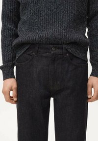 Jeans de mezclilla azul oscuro con corte recto, con detalles sutiles texturizados, bolsillos delanteros y cintura con botones. Suéter con patrón acanalado.