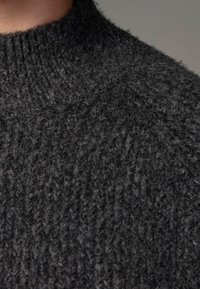 Schwarzer gestrickter Pullover mit hohem Kragen, gerippter Textur und einem weichen, voluminösen Design. Der Stoff wirkt warm und gemütlich.