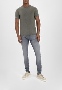 Olivgrünes Baumwoll-T-Shirt mit kurzen Ärmeln und Rundhalsausschnitt, kombiniert mit hellgrauen Slim-Fit-Jeans und beigen Sneakers.