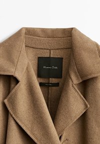 Col et revers en laine marron avec une étiquette noire rectangulaire à l'intérieur indiquant "Massimo Dutti."