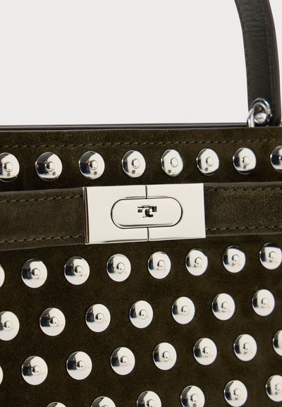 Bolsa de camurça verde escura com tachas redondas prateadas dispostas em filas e um fecho retangular prateado com uma alça.