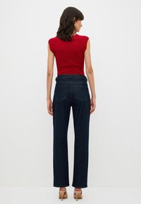 Červený žebrovaný top bez rukávů v kombinaci s tmavě modrými džíny rovného střihu. Džíny mají vysoký pas a dvě zadní kapsy.