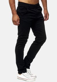 Czarne spodnie slim-fit o gładkiej fakturze, z przednimi kieszeniami i zamkiem błyskawicznym, w zestawieniu z białymi sneakersami dla kontrastu.