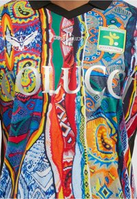 Tricou de fotbal multicolor strălucitor cu modele complexe, guler negru, logo-uri inclusiv emblema Fussballclub Kitzbühel și brandingul "COLUCCI" pe piept.