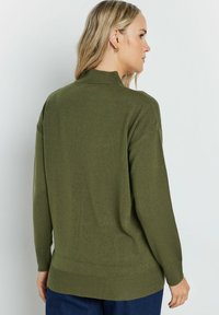Maglione lavorato a maglia verde oliva con un collo alto, maniche lunghe e dettagli a costine sui polsini e sull'orlo. Texture morbida e vestibilità rilassata.