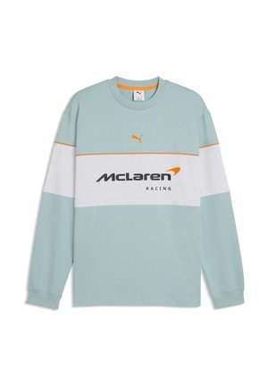Jasnoniebieska koszula z długim rękawem z białym poziomym paskiem, pomarańczowym logo Puma powyżej oraz czarnym i pomarańczowym napisem McLaren Racing na piersi.