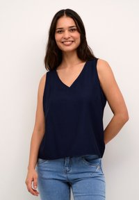 Top fără mâneci de culoare bleumarin, cu decolteu în V, croială lejeră, textură netedă și luciu subtil. Asortat cu blugi din denim de culoare albastră deschisă.