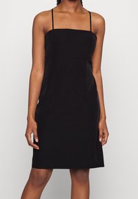 Black fitted dress with thin straps, square neckline, and a smooth, matte texture. Knee-length with a streamlined silhouette and no patterns.