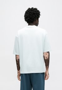 Ανοιχτό μπλε βαμβακερό t-shirt με χαλαρή γραμμή, κοντά μανίκια και ριμπ λαιμόκοψη, απεικονίζεται από πίσω σε λευκό φόντο.