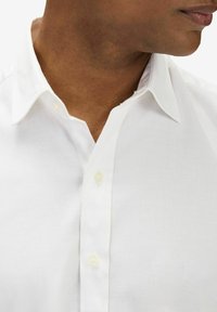 Valkoinen nappikauluspaita, jossa on sileä pinta, klassinen kaulus ja helmiäisvalkoiset napit. Lähikuva kauluksesta ja yläkankaasta.
