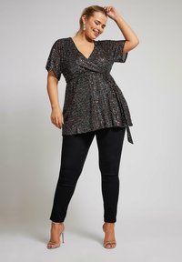 Sort glitrende indpakningsbluse med korte ærmer, der har en bundet talje, parret med sorte slim-fit jeans og strømpesandaler i sølv.