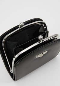 Portefeuille en simili cuir noir avec une fermeture à pince en argent, comportant plusieurs emplacements pour cartes et un revêtement texturé noir.