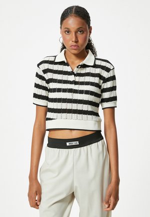 Mujer con cabello rizado que lleva un polo de punto de manga corta a rayas blancas y negras y pantalones claros con una cintura negra con la etiqueta "Unique Plans".