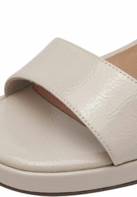 Beige, patentleren slidesandaal met een brede bovenvoetband en een gestructureerde zool. Gladde afwerking met zachte cushioning zichtbaar eronder.