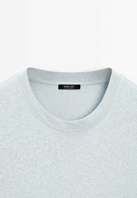 Světle šedé bavlněné tričko s kulatým výstřihem, texturovanou tkaninou a štítkem s nápisem "Massimo Dutti." Hladká textura a jednoduchý design.