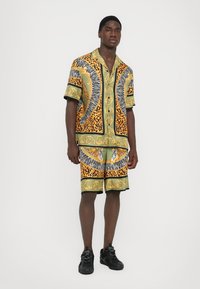Kortärmad skjorta och shorts set i grön, gul och svart med intrikata djur- och blommönster. Tillverkad av lättvikts, mönstrad textil.