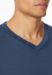 T-shirt blu navy a scollo a V con maniche corte, caratterizzato da una morbida texture di cotone e una silhouette aderente, che mette in risalto le cuciture lisce lungo il collo.