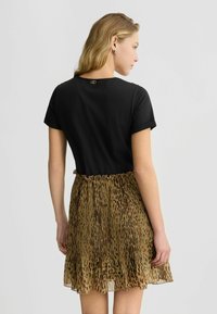 Maglietta nera con maniche corte arrotolate, abbinata a una gonna a pieghe in stampa leopardata marrone e oro, con vita elasticizzata.