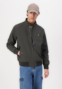 Giacca zip-up grigia scura con colletto alto, polsini a costine e tasche laterali. Presenta un piccolo logo giallo sul lato sinistro del petto.