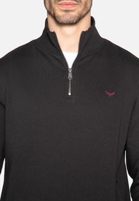 Pullover nero con zip a un quarto realizzato in tessuto morbido, con un sottile logo color maroon sul lato sinistro del petto e un accento in metallo sulla zip.