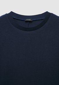 Maglione blu navy con collo rotondo e polsini a coste. Realizzato in un materiale morbido con una texture liscia, design minimalista. Etichetta del marchio visibile.